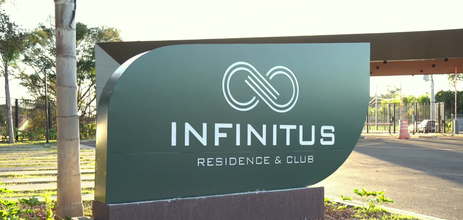 Letreiro de entrada do Infinitus Residence e Club em fim de tarde, com a portaria ao fundo